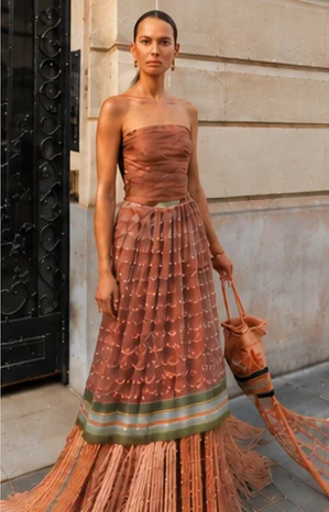 A woman in a strapless terracotta gown with a patterned, fringed skirt