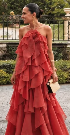 A woman in a red-coral gown of cascading ruffles